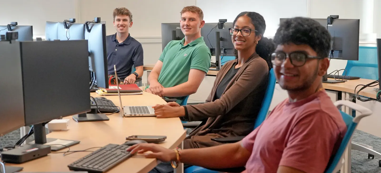4 CyberTrust interns smiling and sitting at computer workstations in an office.