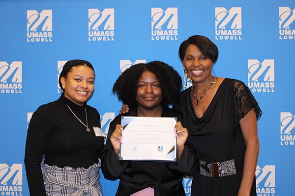 A young woman holds a certificate while posing for a photo with two other women