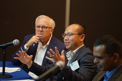 A man in glasses gestures with his hands while speaking as another man looks on