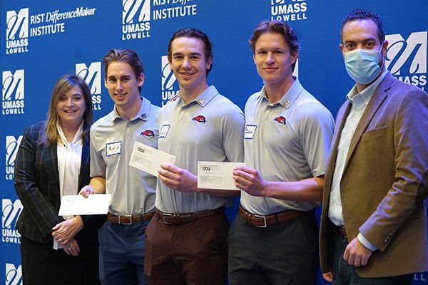 A woman, three male students, and a man pose for a group photo. The students are holding checks.
