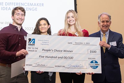 A male student, two women students, and a man hold an oversized check