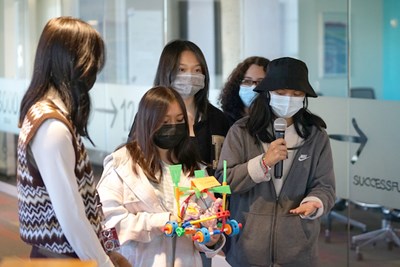 Five female students present a Tinkertoy creation they built, one of them is holding a microphone