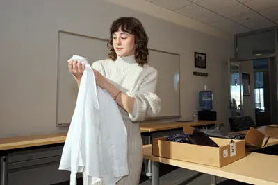 A young woman looks at a white blouse that she is holding while standing in a conference room.