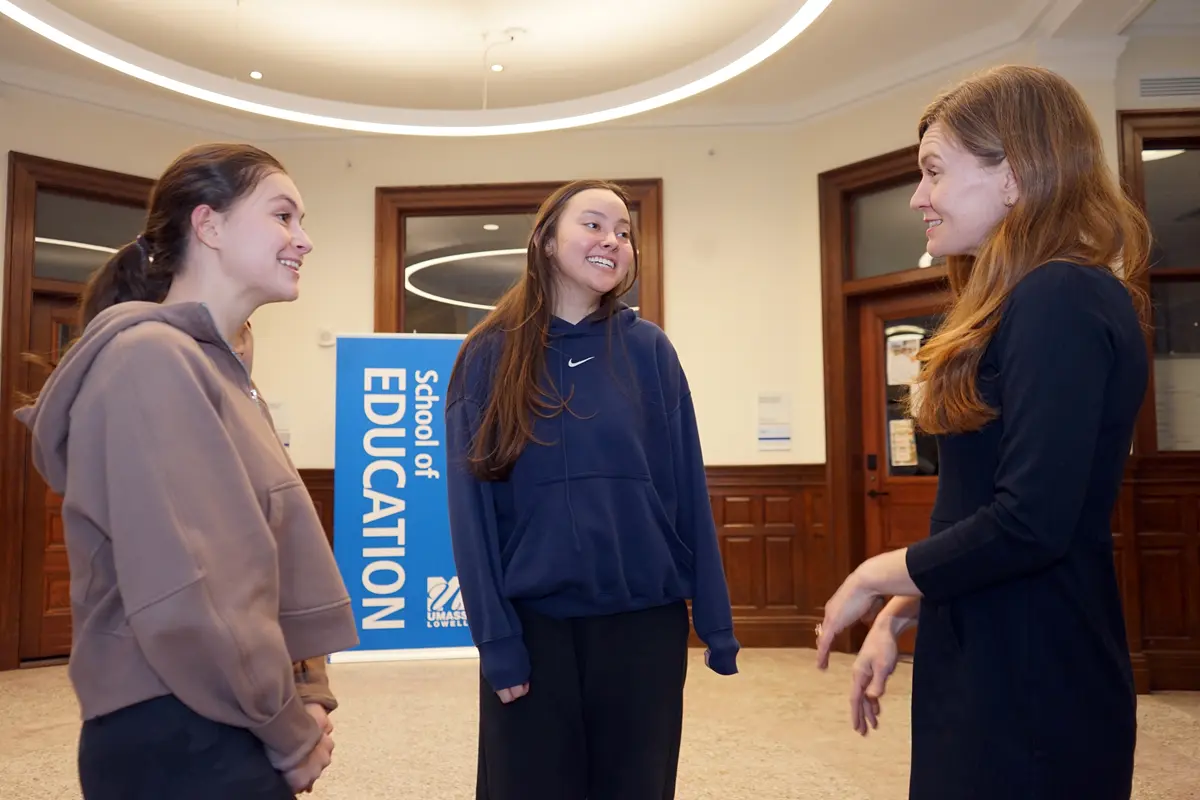 Three women talk in the hallway of an academic building.