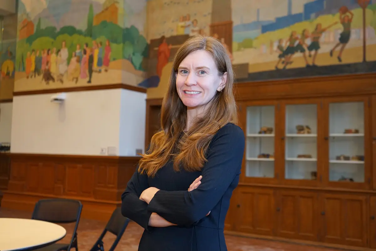 A woman poses for a photo with her arms folded while standing in a room with a mural behind her.
