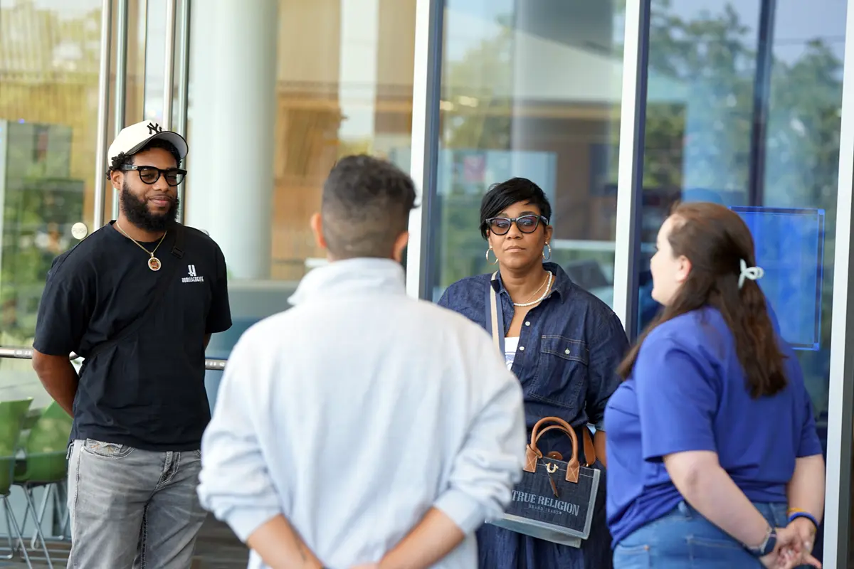 A young man and a woman talk to two people in a room with a glass wall.