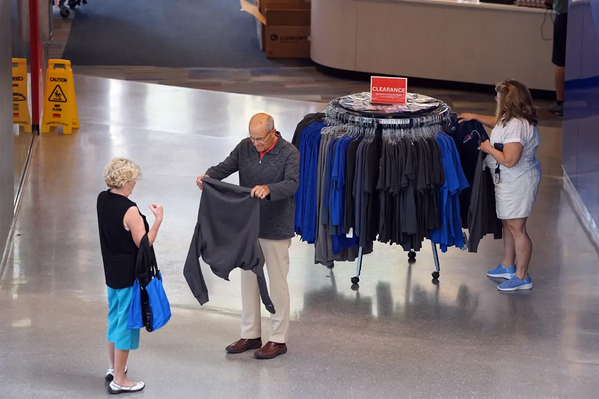 A man and two women look at clothes on a store rack in the lobby of a building.