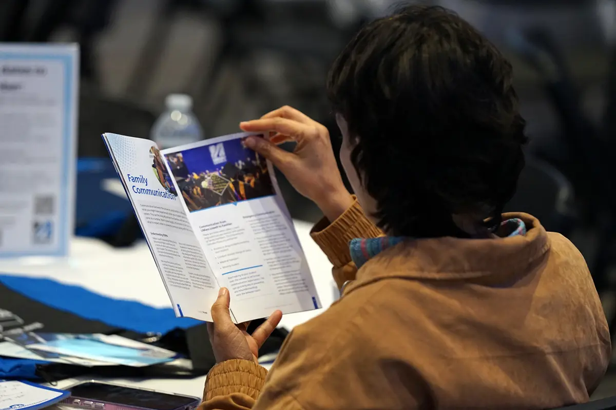 A woman with short dark hair reads a brochure while seated at a table.