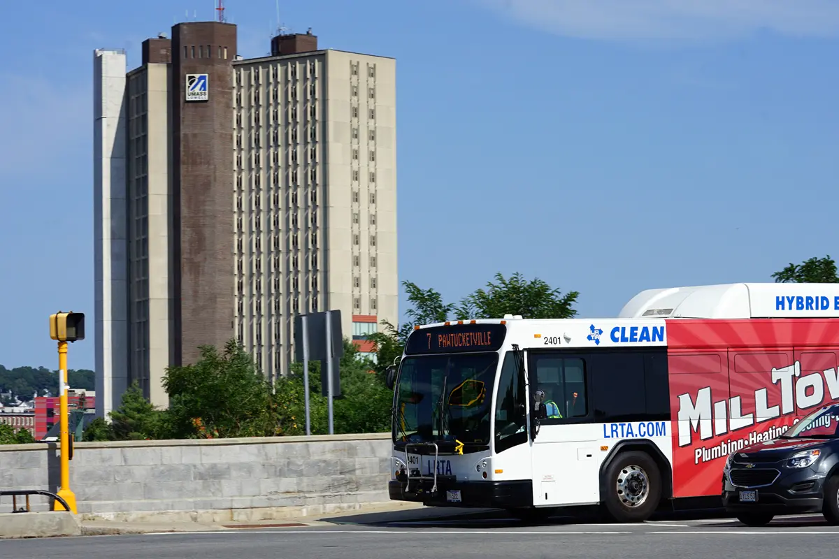 A city bus turns at an intersection. There is a college dorm building in the background.