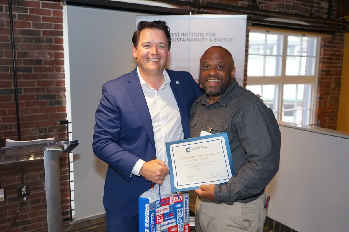 A man holds a certificate while posing for a photo with another man who is holding a gift bag.