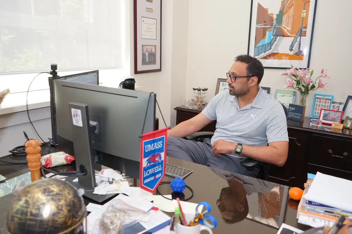 A man in a polo shirt and glasses works at his computer at a desk.