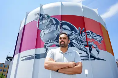 A man with his arms folded stands in front of a nuclear reactor that has a silver crab painted on it.