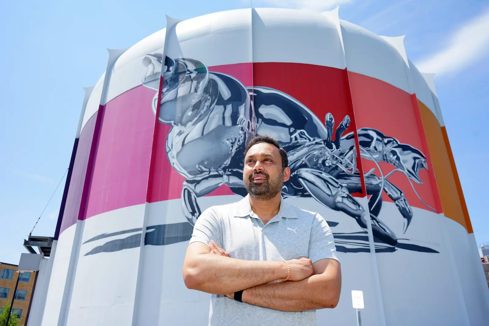 A man with his arms folded stands in front of a nuclear reactor that has a silver crab painted on it.