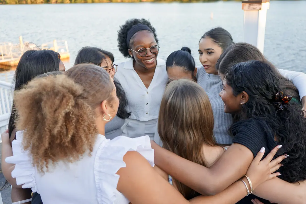 Students hugging in circle at outdoor event.