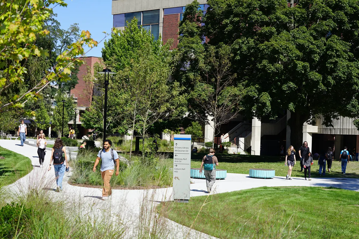 College students walk across a campus plaza on a sunny morning.