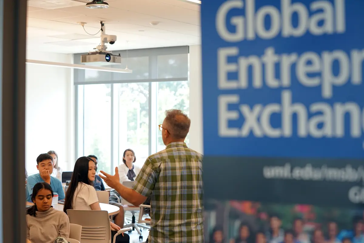 Director Richard Juknavorian teaching in a classroom adjacent to Global Entrepreneurship Exchange sign.