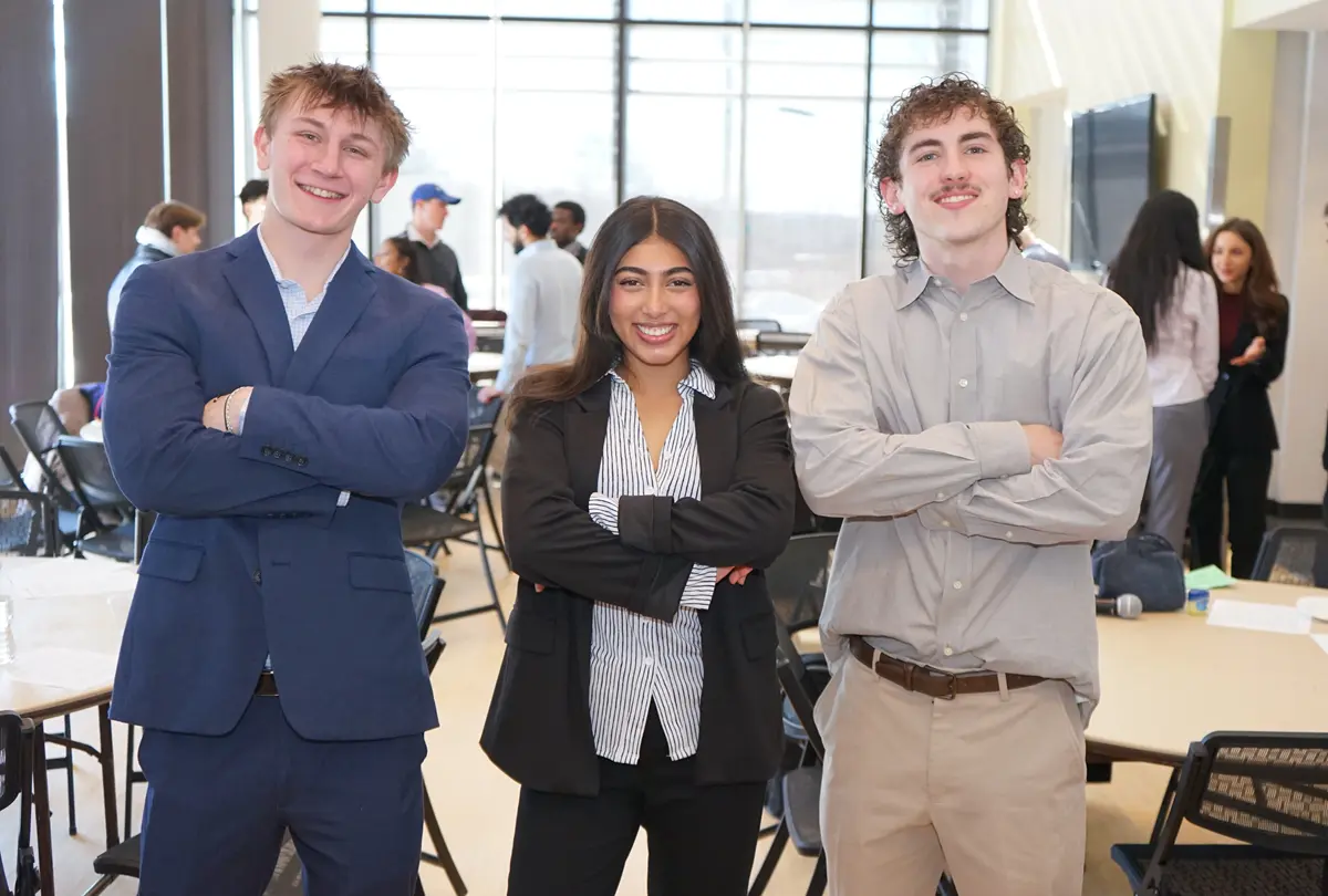 Two young men and a young woman pose for a photo with their arms folded.