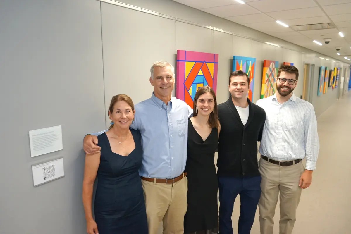 A family of two women and three men pose for a photo in a hallway with artwork on the wall.