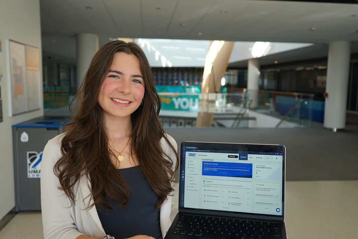 A young woman poses for a photo while holding a laptop.