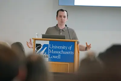 A young man gesturs with his hands while speaking at a podium.