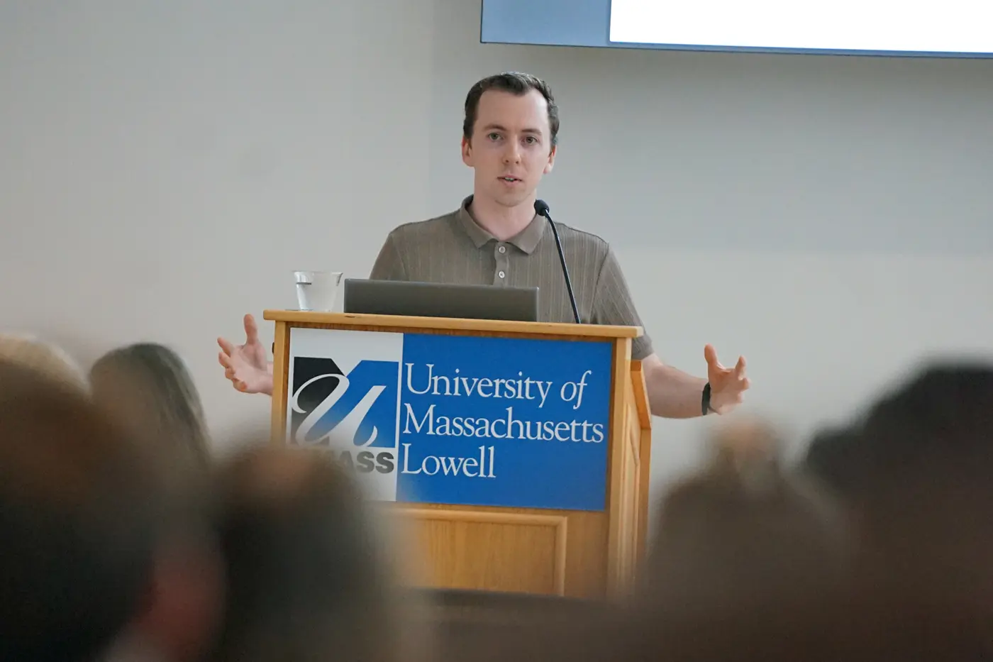 A young man gesturs with his hands while speaking at a podium.