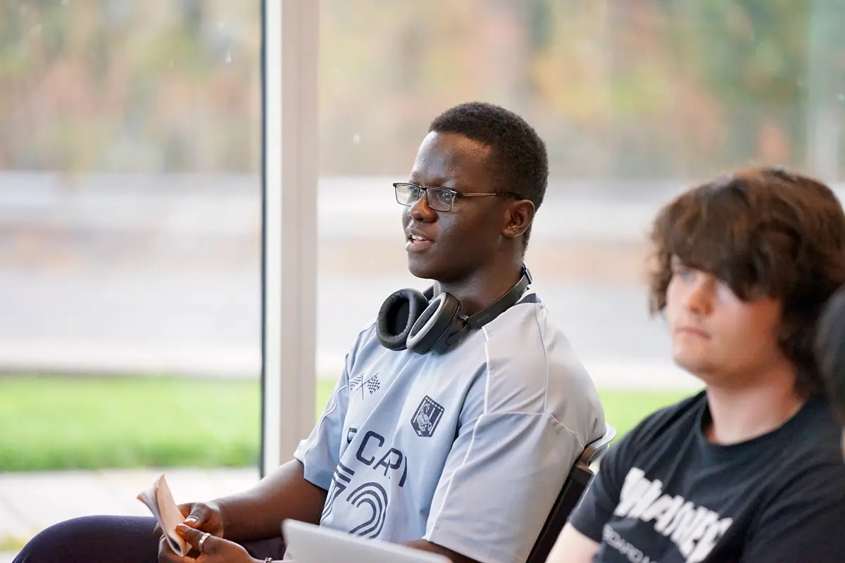 A young man in glasses with headphones around his neck talks while seated.