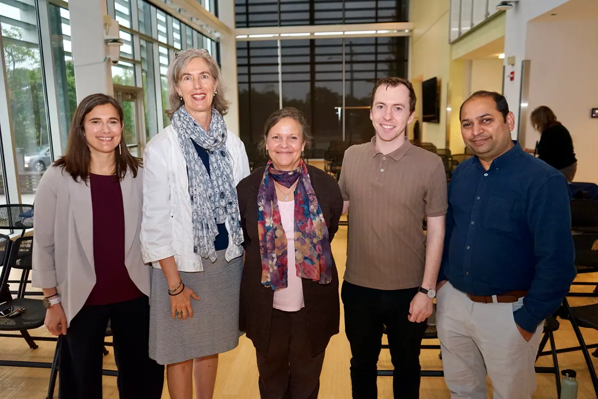 Three women and two men pose for a group photo in a lecture room.