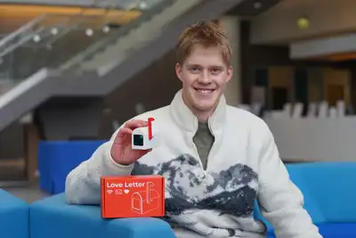 A young man holds a small mailbox device while posing for a photo in a lobby.