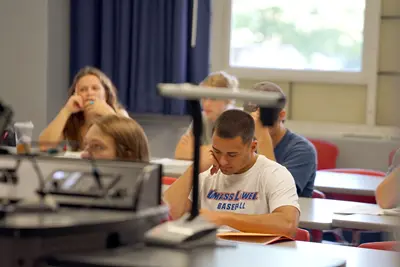 Students at tables in classroom. One wears a UMass Lowell Baseball shirt.