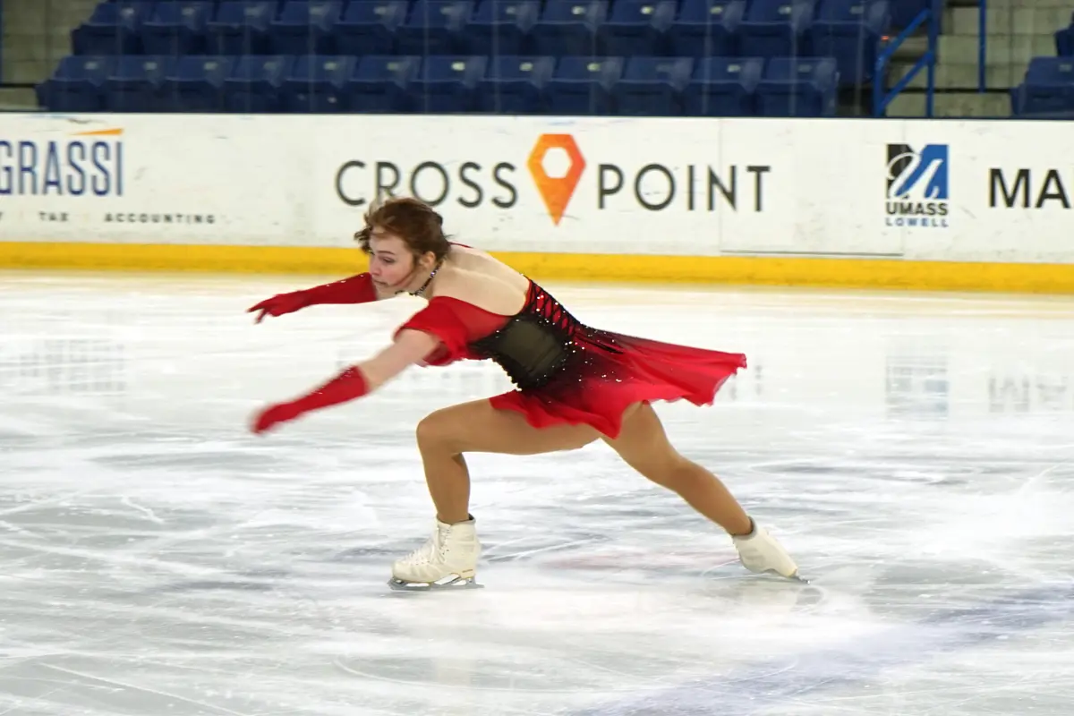 A figure skater in a red outfit performs on the ice.