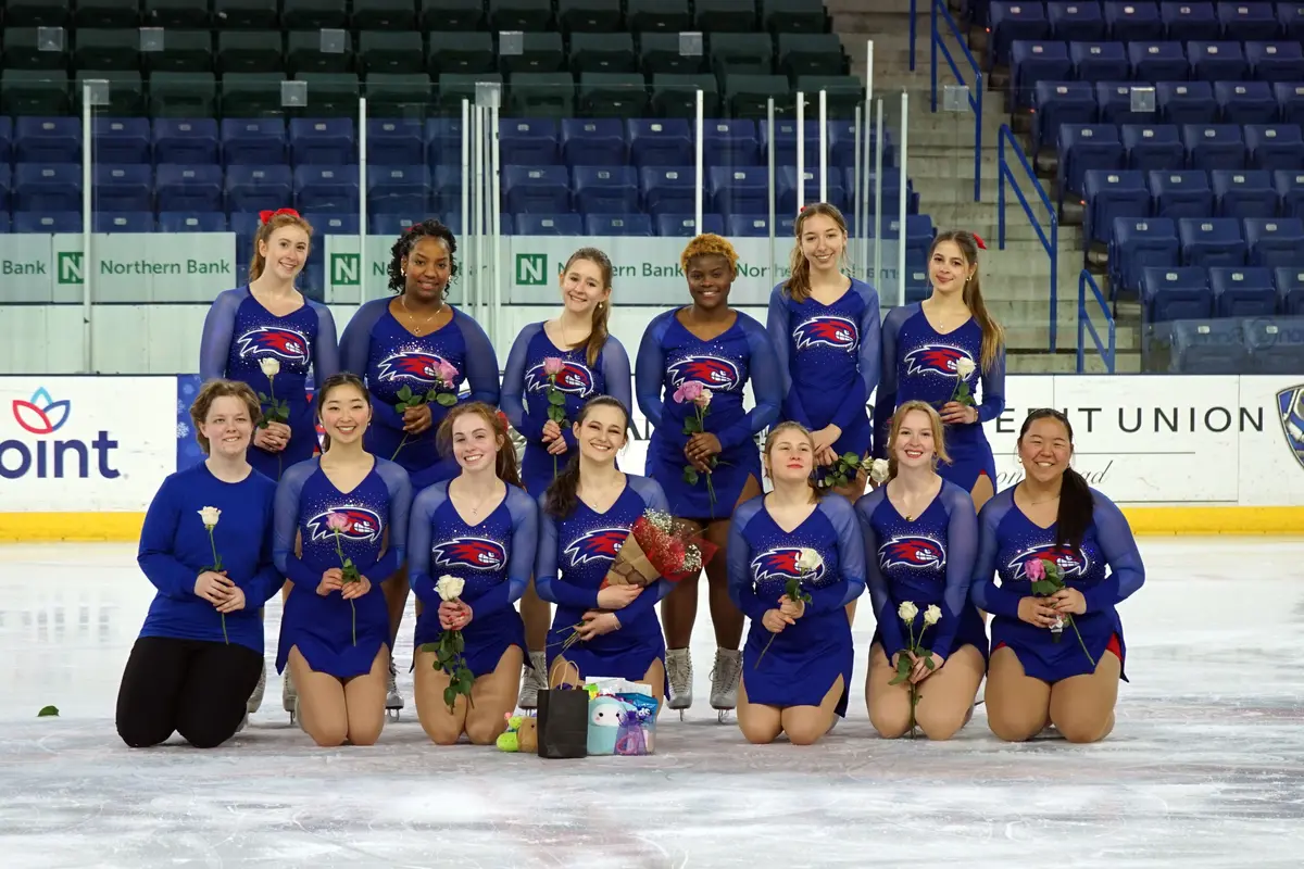 A figure skating team in blue outfits poses for a photo on the ice.