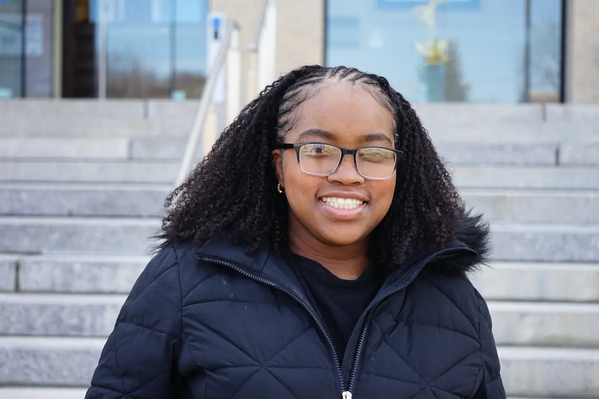 A young woman with dark hair and glasses poses for a photo outdoors in front of stone steps.