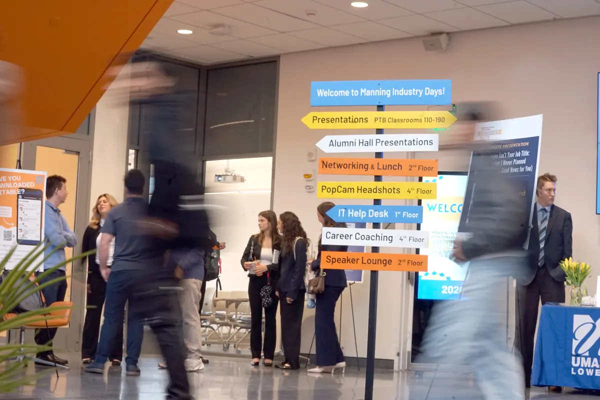College students walk in a lobby past colorful signage pointing to conference sessions.
