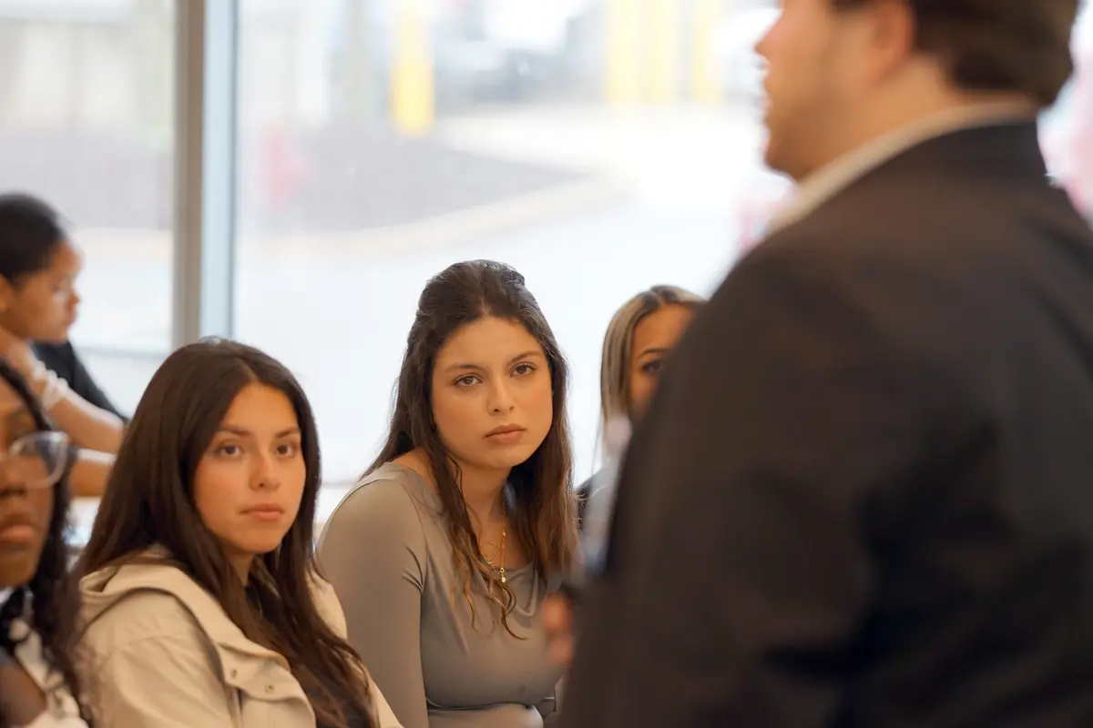 A row of college students look toward a person who is speaking in a classroom.