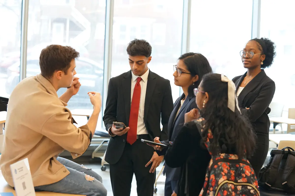 A young man gestures with his hands while talking to a group of college students in a classroom.