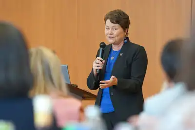 Provost Lynne Cossman holding a microphone and speaking to people in a room.