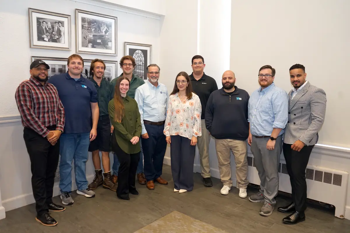 Eleven men and women pose for a group photo in the corner of a room.