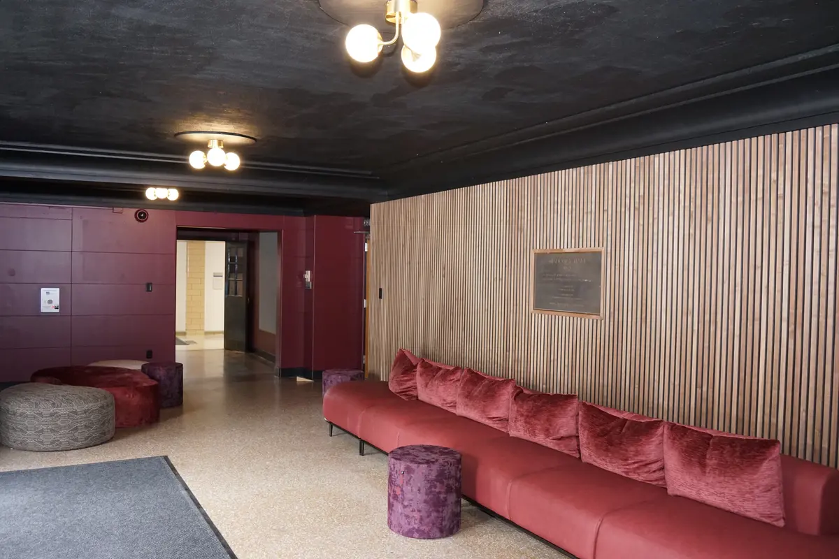 A recently renovated lobby of a theatre with a long red couch and a round ottoman.