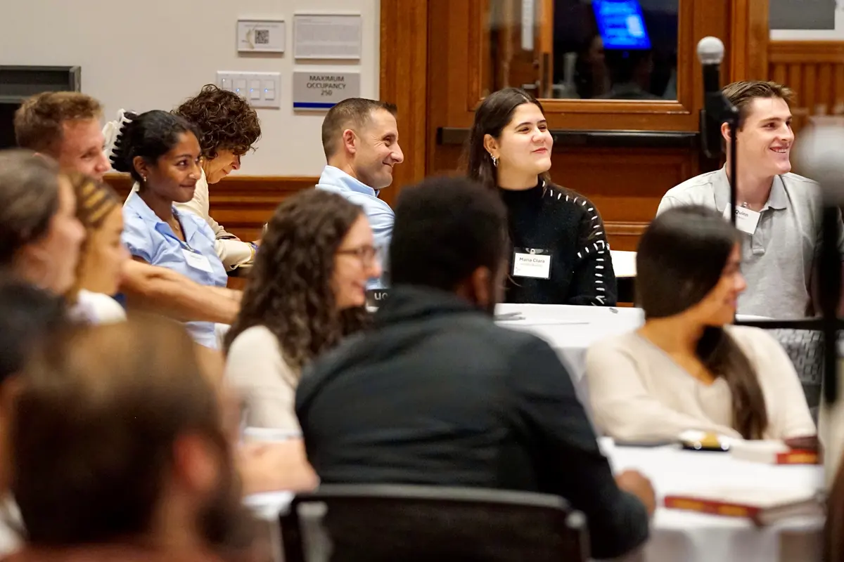 Several people seated at a tables smile while listening to a person talk.