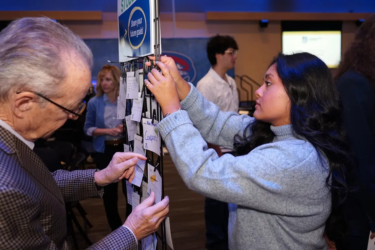 A man with glasses and a young woman clip notes on opposite sides of a metal lattice.