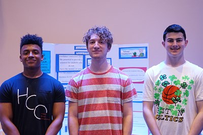 UMass Lowell honors students and business majors Barry Burrell and Anthony Fisher and business major Sam Nardozzi display a poster from a service-learning section of College Writing II