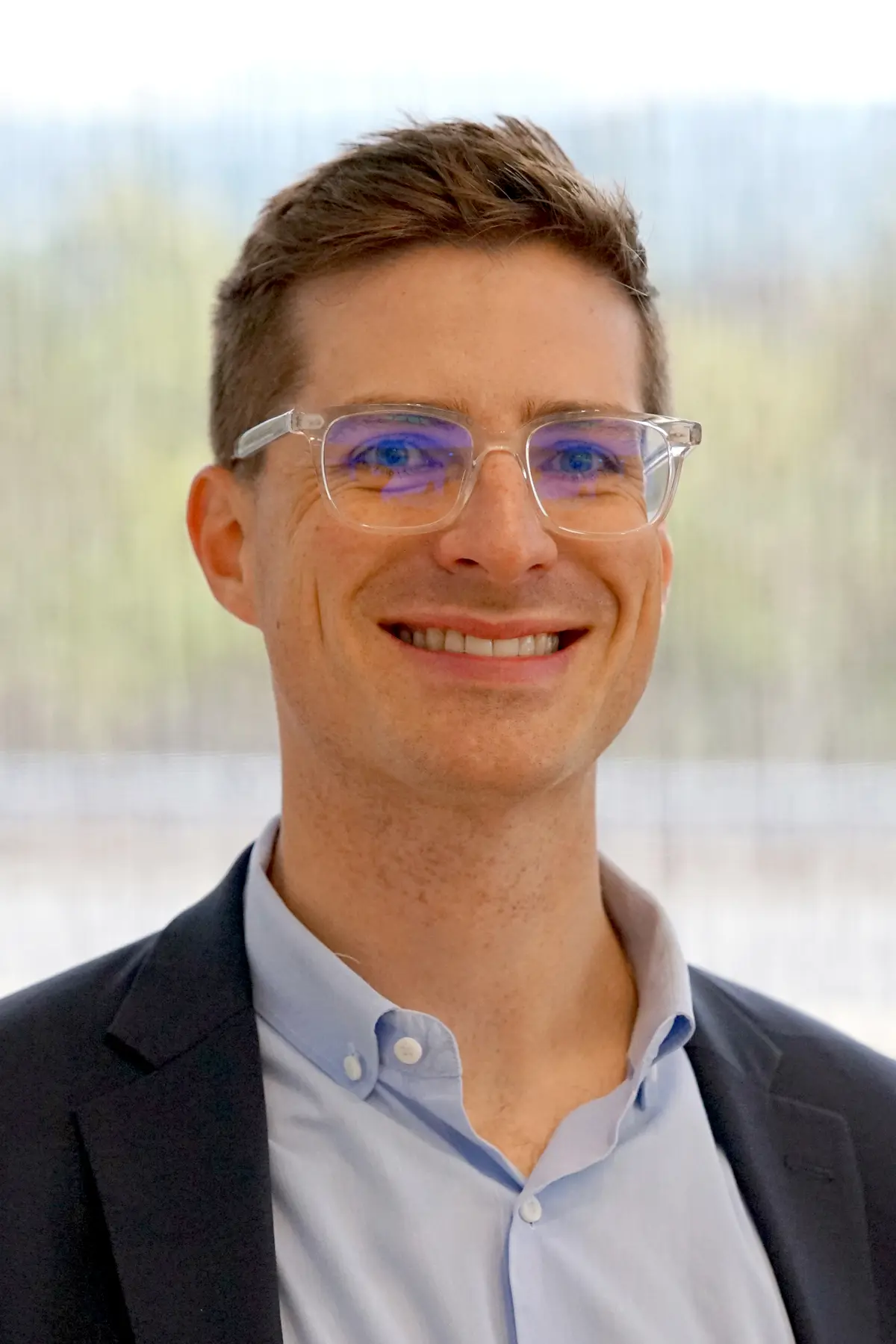 A man with short dark hair and glasses poses for a headshot photo.