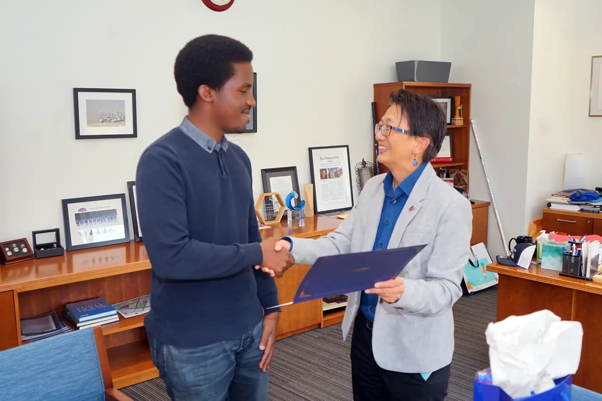 A young man and a woman in a blazer shake hands in an office.