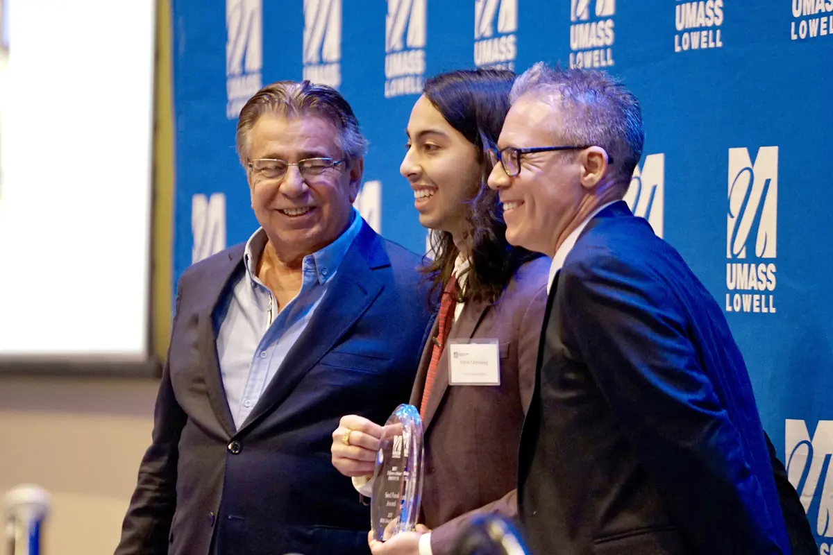 A young man poses for a photo holding a glass award while flanked by two men.