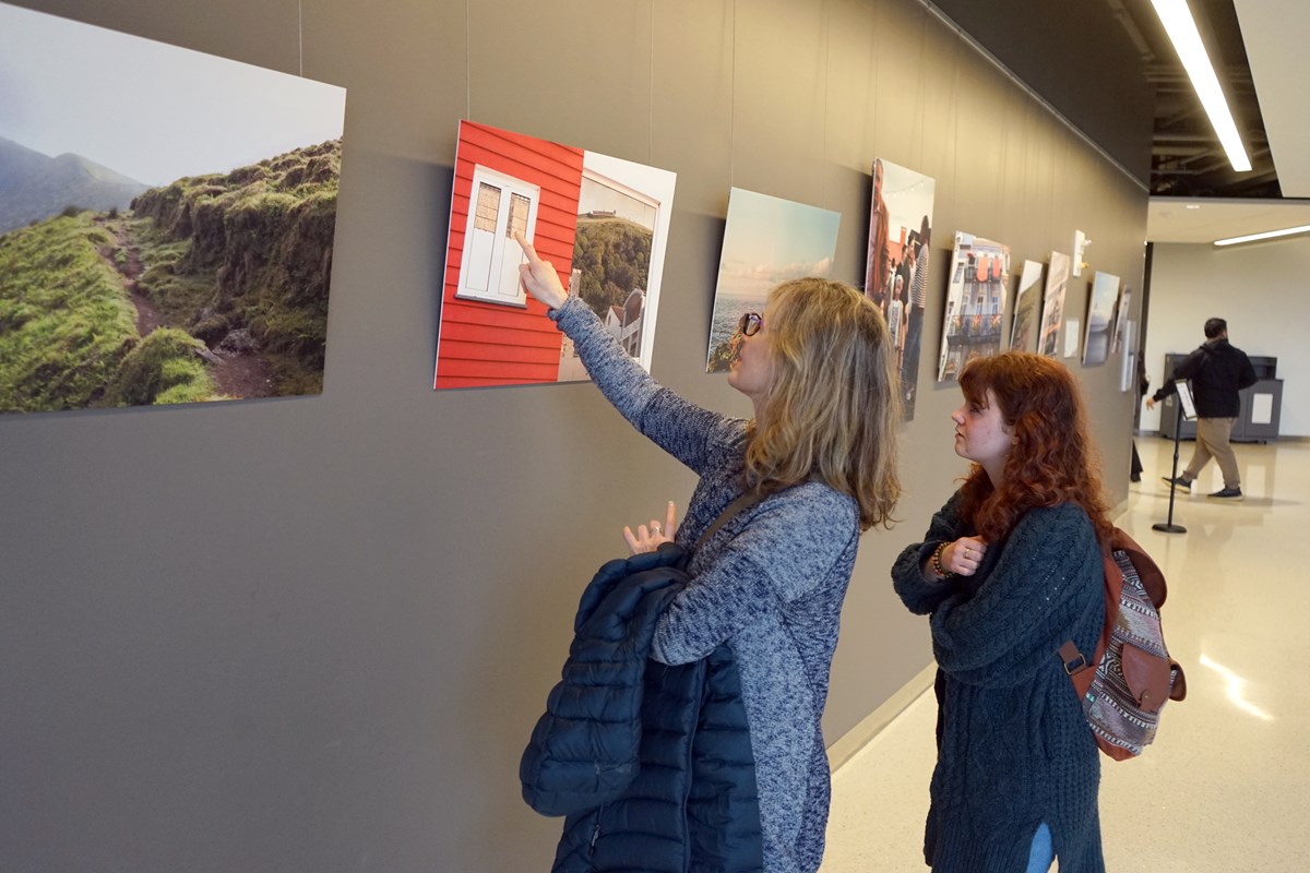 A person points at a photo hanging on an exhbit wall while another person looks on.