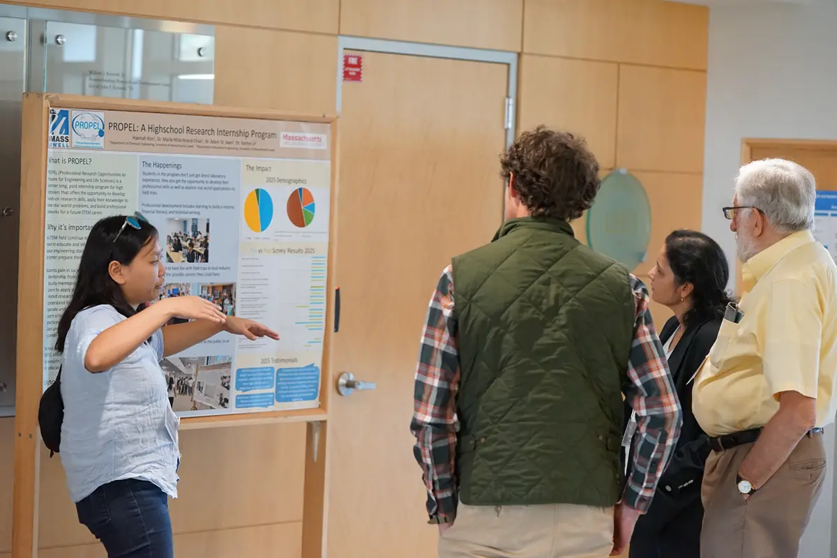 A woman gesures with her hands while talking to three people while standing in front of a research poster.