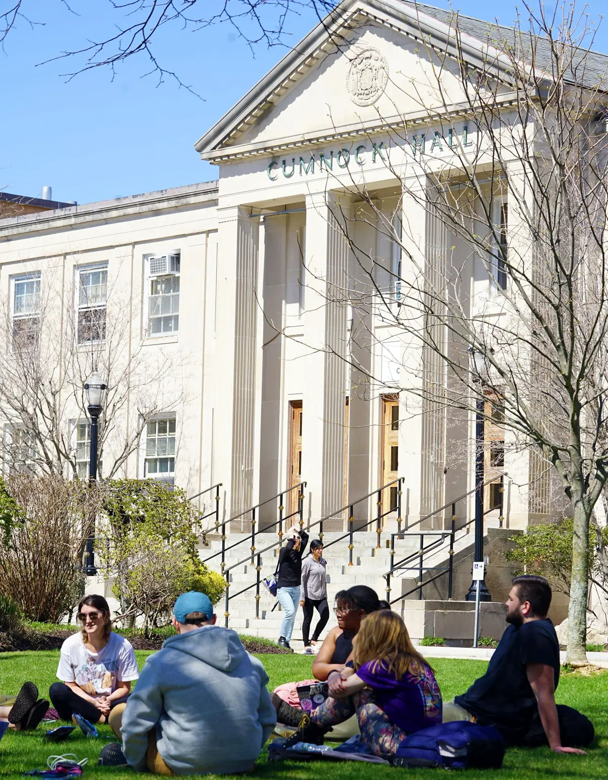 Students sit in a circle on the lawn in front of Cumnock Hall