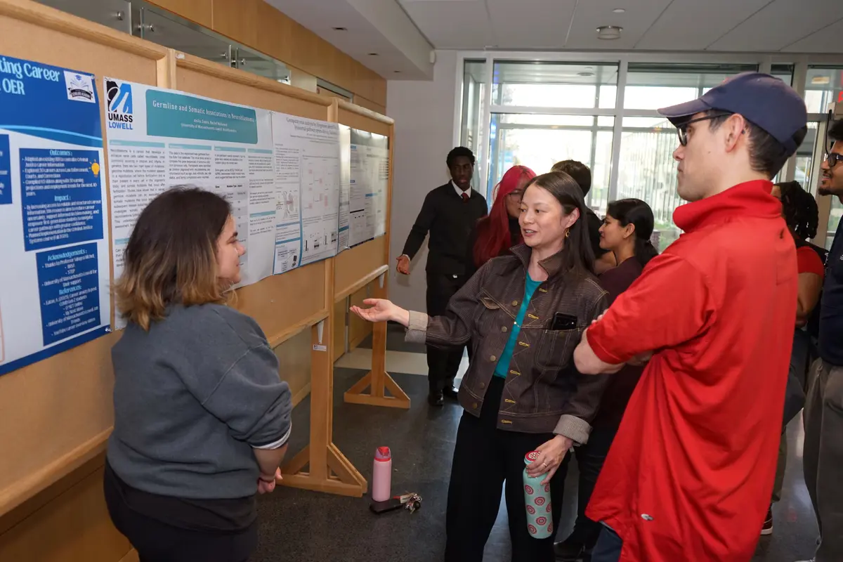 Three people stand in front of a research poster and talk in a room.