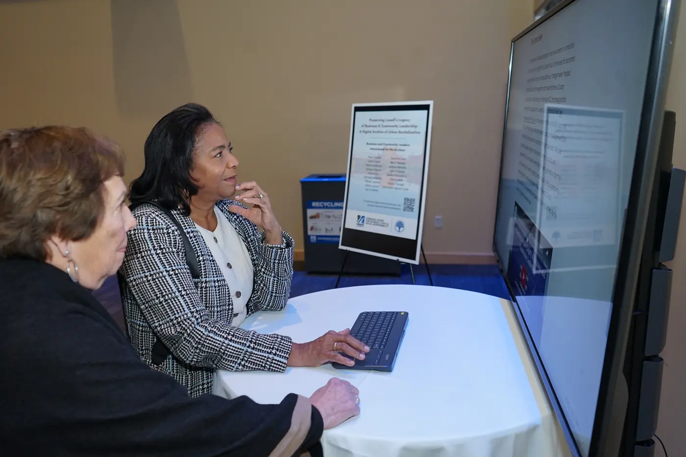 A woman looks at a computer screen while another woman looks on.