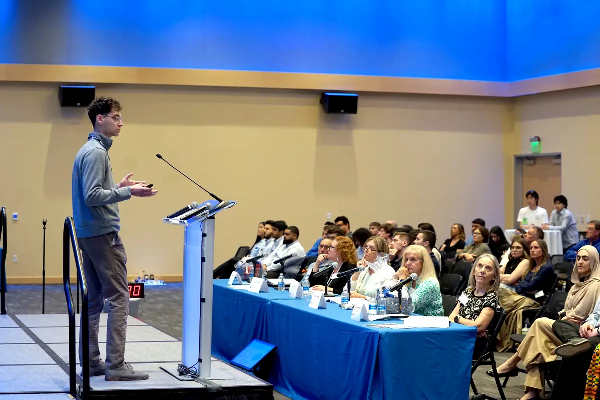 A young man on a stage gives a presentation to a room full of people.